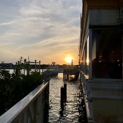 Scenic view of canal by buildings against sky during sunset