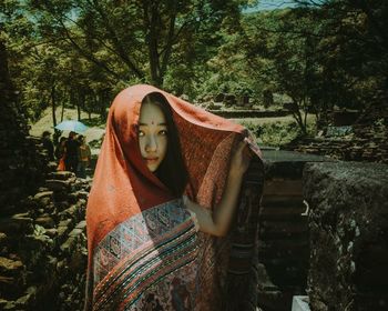 Portrait of young woman wearing scarf against trees on field