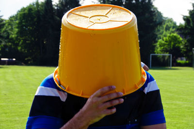 Man with face covered by yellow bucket on soccer field