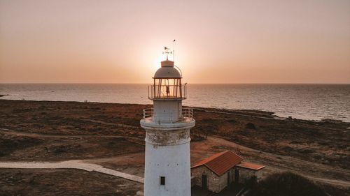 Lighthouse by sea against sky during sunset