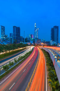 Light trails on road amidst buildings in city against sky