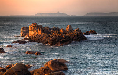 Rocks on sea shore against sky during sunset