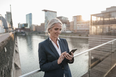 Smiling businesswoman using cell phone on bridge