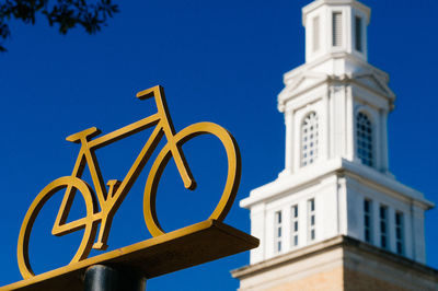 Low angle view of artificial bicycle by building against clear blue sky