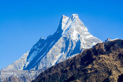 Low angle view of snowcapped mountains against clear blue sky