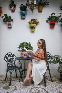 Graceful female in skirt leaning legs on chair while chilling in patio in summer and enjoying interesting story in book at weekend