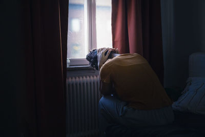 Young woman sitting by window with head in hands