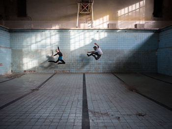 Friends jumping in abandoned empty swimming pool