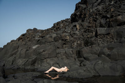 Naked woman lying on rocks by sea