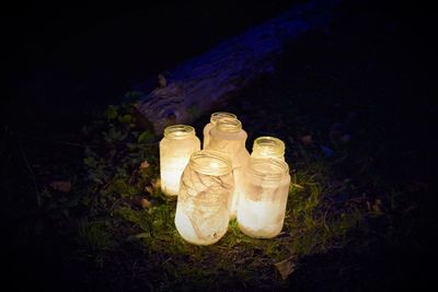 Burning candles in glass jars on field at night