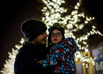 Father carrying son while standing against lights at night