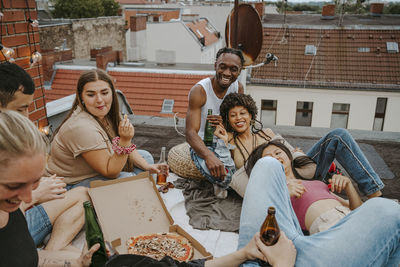 Happy male and female friends with pizza enjoying party on rooftop