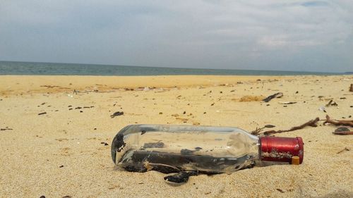 Close-up of bottle on sand at beach against sky