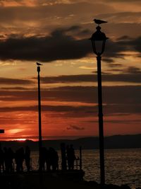 Silhouette people at lakeshore against sky during sunset