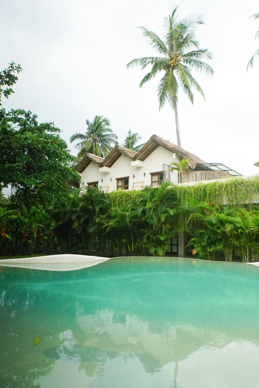 tropical climate, palm tree, water, swimming pool, tree, wealth, architecture, nature, luxury, tourist resort, plant, house, built structure, building, building exterior, travel destinations, trip, vacation, residential district, holiday, resort, tranquility, hotel, estate, sky, tropical tree, beauty in nature, no people, outdoors, tranquil scene, relaxation, home, mansion, luxury hotel, poolside, idyllic, travel, reflection, villa, sea, land, day, home ownership, green, tourism, scenics - nature, coconut palm tree, summer, environment, front or back yard, beach, island