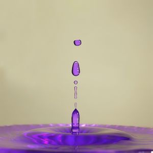 Close-up of drop falling on pink water against gray background