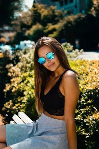 Portrait of woman in sunglasses sitting against plants