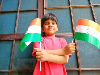 Portrait of boy holding indian flags against window