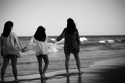 Rear view of friends standing on beach against sky