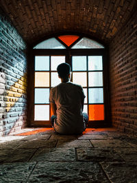 Rear view of man sitting on wall of building