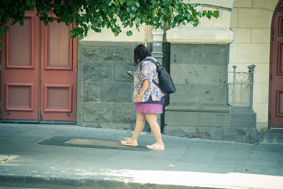 Full length rear view of woman walking on footpath against building