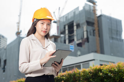 Young woman using mobile phone while standing against buildings