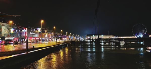 Illuminated street by city against sky at night