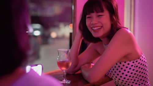 Smiling woman with drink sitting at illuminated nightclub