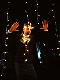 Portrait of man wearing illuminated lights while standing in darkroom