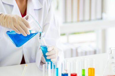 Midsection of scientist pouring blue liquid in test tube at laboratory