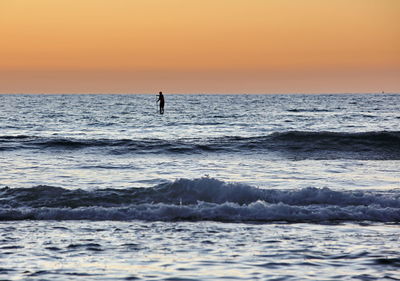 Silhouette person in sea against sky during sunset