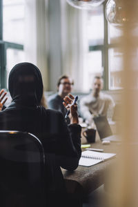 Rear view of young entrepreneur discussing with colleagues sitting at conference table