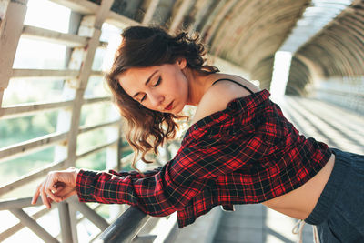 Beautiful female dancer bending on railing at pedestrian bridge