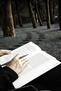 Cropped image of person reading book while sitting on chair at field