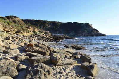 Rocks on beach against clear blue sky