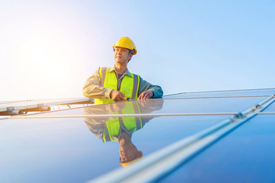 Male engineer repairing solar panels against blue sky