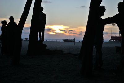 Silhouette people standing on beach at sunset