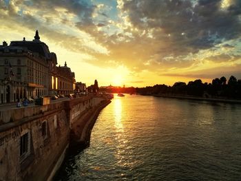 View of river amidst buildings against sky during sunset