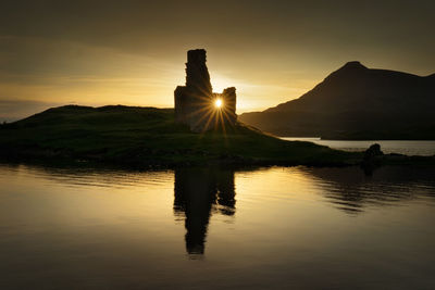 Silhouette built structures by lake against sky during sunset