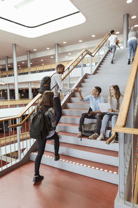 Full length of multi-ethnic students greeting on steps in university campus