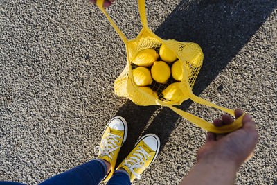 Woman standing on road opening mesh bag with lemons