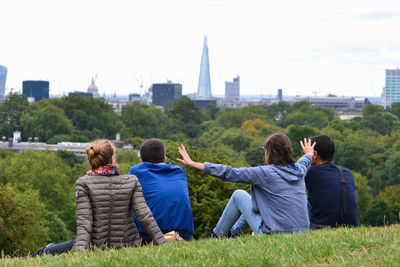 Rear view of woman with arms outstretched standing amidst friends in park