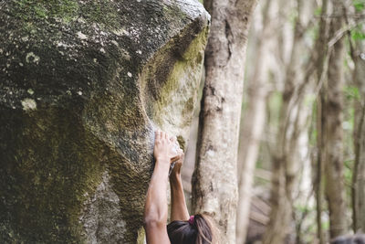 Upper body of a female climber climbing a rock in a forest