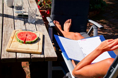 Low section of woman with document sitting on chair at yard