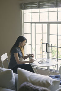 Woman using mobile phone while having coffee at table in living room