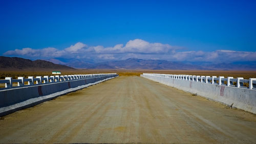 Road leading towards mountain against blue sky