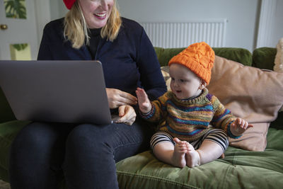 Mother playing with son while using laptop at home