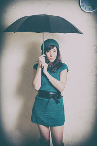 Portrait of mid adult woman holding umbrella while standing against wall