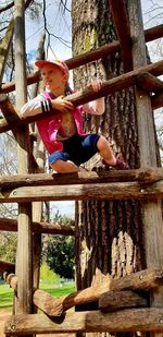 Low angle view of girl playing on wood against trees