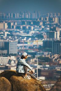 Man sitting in city against sky